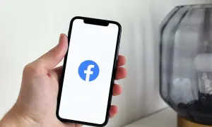 Dłoń trzyma smartfon z logo Facebooka. Dowiedz się, jak dodać zdjęcie profilowe na FB z galerii.