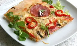 Kawałek pizzy z salami, papryką i serem na białym talerzu. Idealne ciasto na pizzę z chrupiącymi brzegami.
