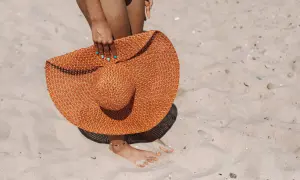 Donna con cappello di paglia arancione sulla sabbia, un'idea per come mantenere l'abbronzatura.