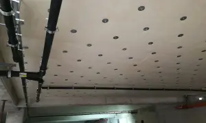 Sufit w garażu z widocznymi rurami kanalizacyjnymi i licznymi okrągłymi elementami mocującymi.