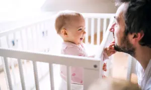 Een lachende baby in een ledikantje reikt naar de baard van haar vader. Pure liefde tussen vader en dochter.