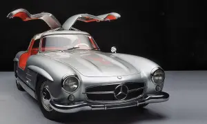 Srebrny Mercedes 300SL z otwieranymi do góry drzwiami, z czerwonym wnętrzem, prezentuje się elegancko na ciemnym tle.