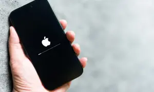 Dłoń trzyma iPhone'a z logo Apple i paskiem postępu. To może być wskazówka, jak wyczyścić pamięć w iPhone, gdy system się ładuje.