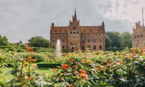 En vacker tegelbyggnad med torn och en fontän i en blomstrande trädgård. En dröm för en vecka på Fyn.