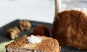 Ein knuspriges Kalbsschnitzel, italienisch zubereitet, mit feinen Beilagen auf einem dunklen Teller.
