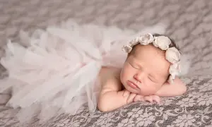 Un bébé endormi, paré d'une couronne de fleurs et d'une jupe en tulle, évoque la douceur et la pureté. Sa pose paisible invite à réfléchir à la signification prénom.