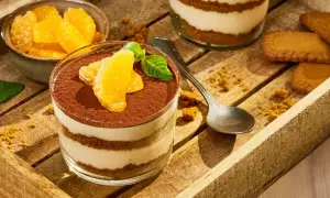 Délicieux tiramisu aux fruits d'orange, garni de cacao et de menthe fraîche, servi dans un verre sur un plateau en bois avec des biscuits.