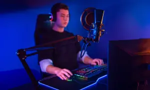Ein junger Mann mit Kopfhörern sitzt vor einem beleuchteten Mikrofon und einer Tastatur. Er ist ein Twitch Streamer, der seine Spiele oder Inhalte live teilt.