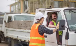 Deux ouvriers du BTP discutent près d'un camion. L'un d'eux, au volant, sourit. Discussion sur le paiement des heures de route dans le BTP.