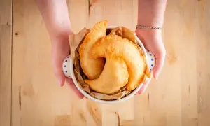 Mani che offrono un cestino di frittelle dorate, un sapore autentico di street food pugliese.