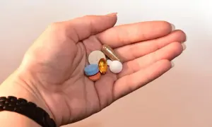 Dłoń trzyma garść tabletek i kapsułek, w tym pomarańczową, owalną, przypominającą levonor.