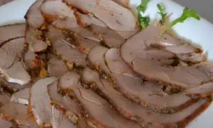Pokrojony pieczony udziec z indyka z kością i skórą, przyprawiony ziołami, ułożony na białym talerzu.