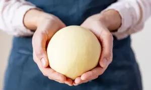 Hände halten einen runden, hellgelben Teigball.
