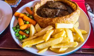 Pyszne danie kuchni brytyjskiej: pieczeń wołowa w Yorkshire puddingu, podana z frytkami, groszkiem i marchewką.