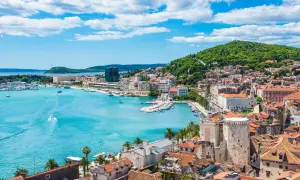 Widok na Split z turkusową wodą, łodziami i zielonym wzgórzem. Ciekawe chorwackie miasto pełne historii.