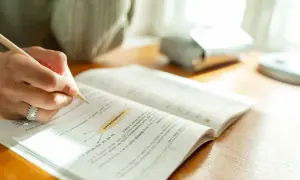 Mano escribiendo en un libro abierto, concentrada en la lectura B2.