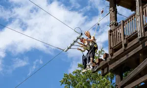 Dwie kobiety na tyrolce w parku linowym na tle błękitnego nieba z chmurami.