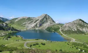 Lago Ercina en la montaña de Covadonga, rodeado de verdes prados y picos rocosos bajo un cielo azul.