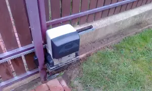 Silnik bramy przesuwnej, która po zamknięciu sama się otwiera, z widocznym zębatką i mechanizmem.