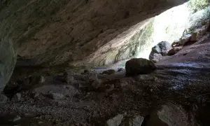 L'interno di una grotta con rocce sparse e un'apertura luminosa che rivela la valle scappuccia.