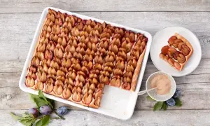 Ein köstlicher Zwetschgenkuchen vom Blech, mit saftigen Pflaumen belegt und goldbraun gebacken. Daneben ein Stück Kuchen auf einem Teller.