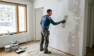 Man spacklar en vägg, torktid spackel innan målning. Verktyg och färgburkar står på golvet.
