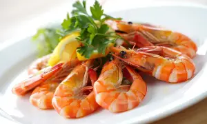 Deliciosas gambas al ajillo servidas en un plato blanco, adornadas con perejil fresco y rodajas de limón.