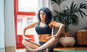 Mujer practicando hipopresivos postparto en casa, sentada en el suelo con las piernas cruzadas.
