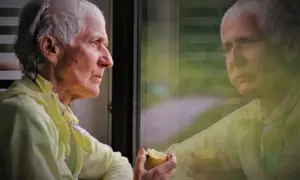 Äldre kvinna med grått hår äter ett äpple vid ett fönster, reflekterad i glaset. Kanske en stund av eftertanke kring quetiapin och depression.