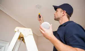 Un technicien installe des alarmes incendie au plafond, assurant la sécurité de votre domicile.