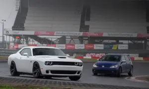 Biały Dodge Challenger i niebieski Volkswagen Golf na torze Słomczyn. W tle trybuny i banery reklamowe.
