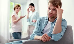 Młody mężczyzna zamyślony, podczas gdy dwie kobiety w tle dyskutują, być może o odrzuceniu spadku a wezwaniu do sądu.