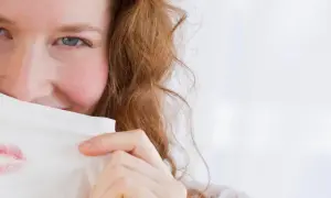Frau mit roten Haaren versteckt sich hinter einem Tuch mit Lippenstiftflecken. Ein Beispiel, wie man Lippenstiftflecken entfernen kann.