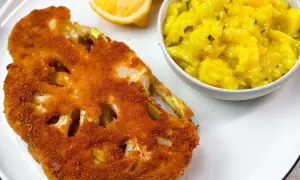 Knuspriges Blumenkohl-Schnitzel mit Kartoffelsalat und Zitronenspalten auf einem weißen Teller.