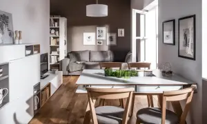 Mała jadalnia inspiracje: nowoczesny salon z szarą kanapą, białymi meblami i drewnianym stołem.