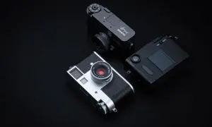 Tre fotocamere Fujifilm X-Half, una argento e due nere, disposte su sfondo scuro.