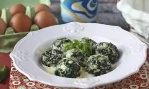 Spenat recept: Krämiga spenatbollar med basilika och parmesan på en vit tallrik. Ägg i bakgrunden.