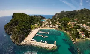 Malownicza zatoka na Korfu, idealna na wakacje z dzieckiem. Widać tu port z łodziami, plażę i zielone wzgórza.