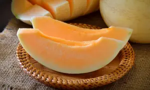 Dwa soczyste kawałki melona, jakby w ciąży, leżą na plecionej podstawce. W tle widać resztę owocu.