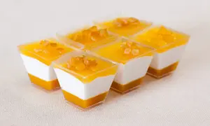Sechs kleine Dessertgläser mit weißer Creme und Mango-Topping, garniert mit kleinen Fruchtstückchen.