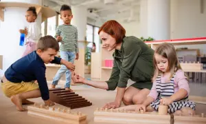 Niños y maestra en el suelo, aprendiendo con materiales didácticos. Las rutinas diarias en el aula fomentan el desarrollo.