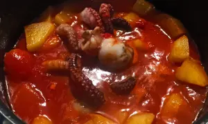 Un saporito stufato di polpo e patate in un sugo rosso brillante. I tentacoli del polpo sono ben visibili, immersi tra i pezzi dorati di patate.