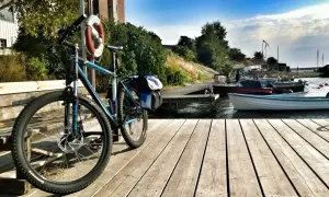 Rower z sakwami czeka na przygodę w Karlskronie. Drewniany pomost, łodzie i błękitne niebo zapraszają do odkrywania uroków wybrzeża.