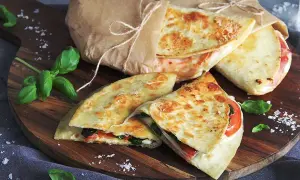 Läckra piadina recept på en träskärbräda, inslagna i papper med snöre. Basilika och flingsalt dekorerar.