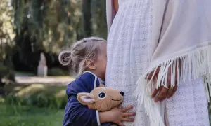 Małe dziecko, tuląc pluszowego jelonka, chowa się za białą sukienką. To obrazek, który pokazuje, jak bardzo wrażliwe dziecko szuka bliskości i bezpieczeństwa.