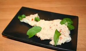 Zarter Fisch mit cremiger Joghurtsoße, garniert mit frischen Kräutern auf schwarzer Platte.