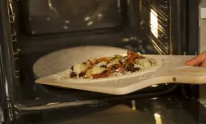 Pizza z dodatkami na łopacie do pizzy, gotowa do wsunięcia na kamień do pizzy granitowy w rozgrzanym piekarniku.