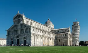 La piazza dei Miracoli a Pisa con il Duomo e la celebre torre di Pisa, simbolo della città, sotto un cielo azzurro.