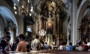 Ludzie uczestniczą w liturgii mszy świętej w bogato zdobionej, barokowej świątyni.