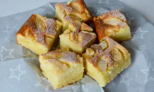 Pyszne ciasto z jabłkami i skyrem, posypane cukrem pudrem, prezentuje się apetycznie na szarej serwetce w gwiazdki.